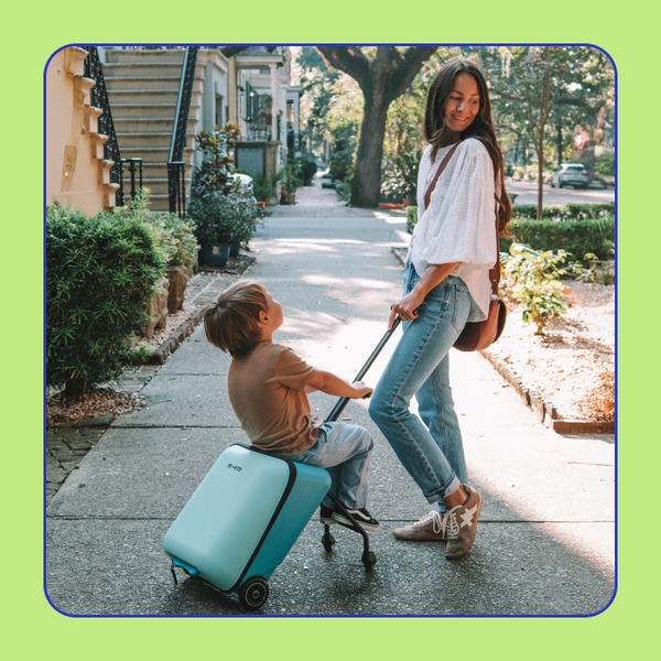 A mom poses with the Micro Allrounder Ride-On Travel Cart while she pulls her son who is sitting on the ride. 