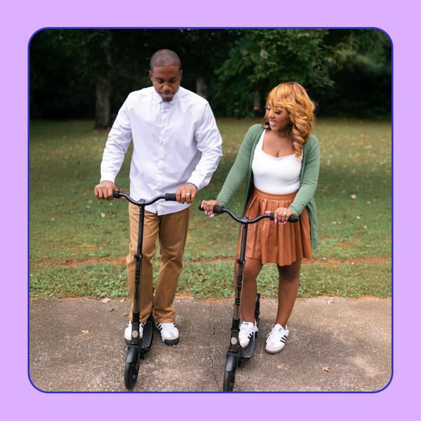 Two adults pose with their Micro Classic Black Neochrome Scooters. 
