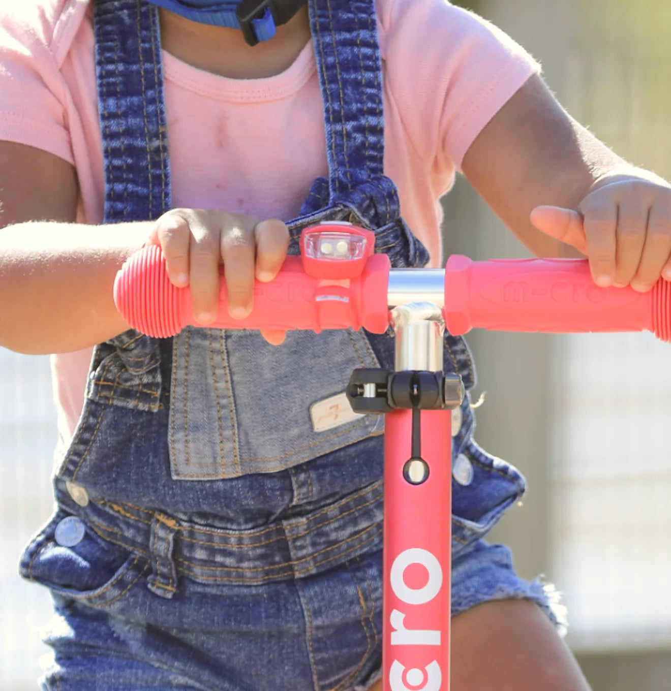Close-up of a child gripping the handlebars of a Micro scooter, featuring a mounted Micro Scooter Light for enhanced visibility and added safety.
