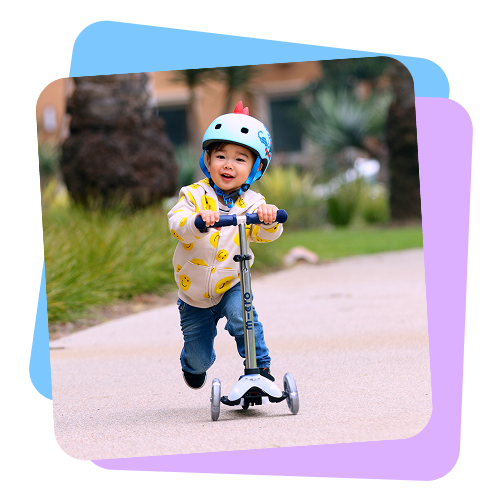 Child riding a scooter with a helmet on a path with greenery in the background