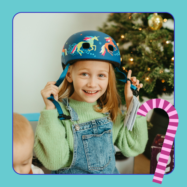 A young girl smiles while putting on her Micro Helmet in the Unicorn design. 