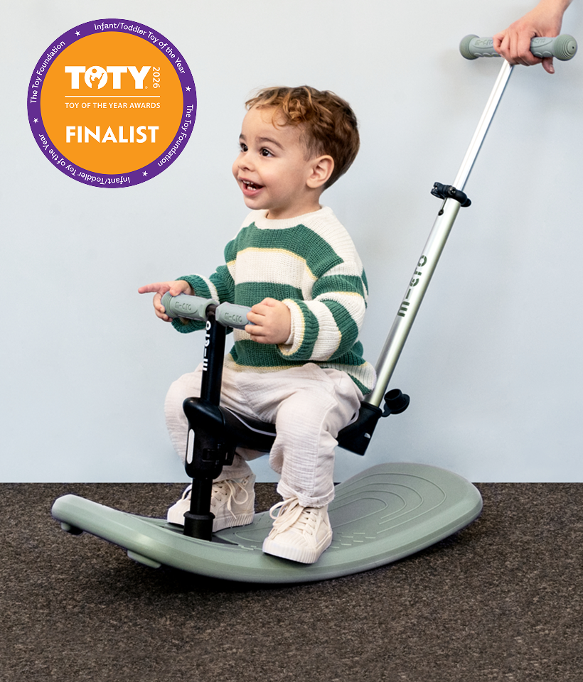 Child using a rocker with parent push bar on a carpeted floor with a plain wall background