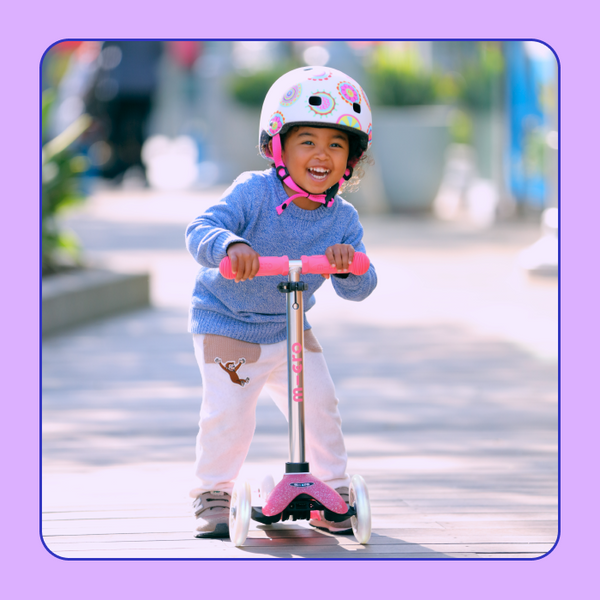 A young girl smiles and poses with the Micro Mini Glitter LED Scooter.