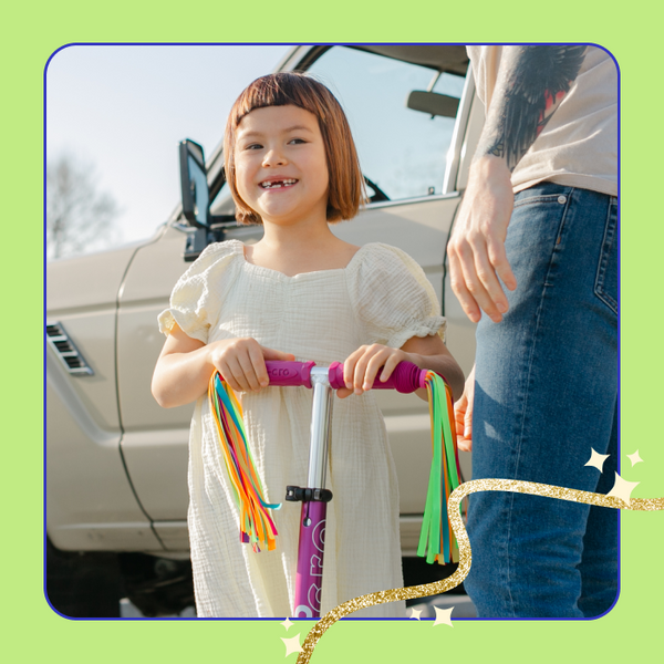 A young girl smiles and poses with her Micro Scooter Streamers attached to her Micro scooter. 